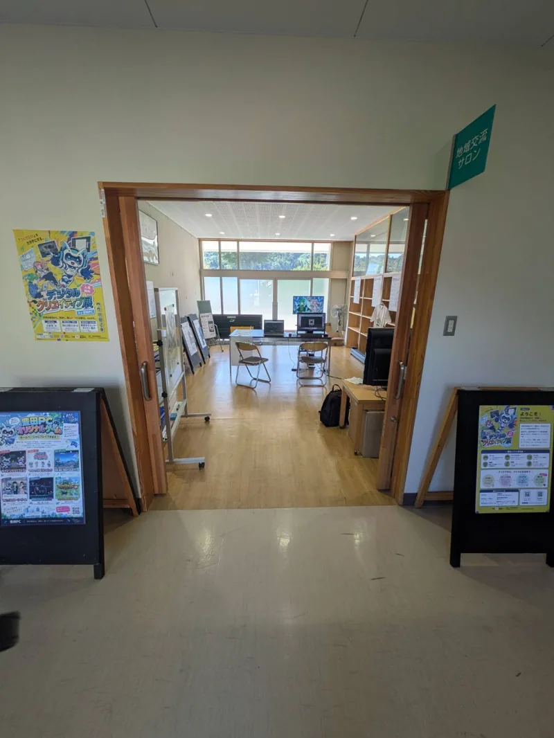 地域交流サロンの入口から見た小鮒祭の展示会場。豊田PCのチラシ、作品紹介パネル、ゲーム用パソコンが並ぶ。